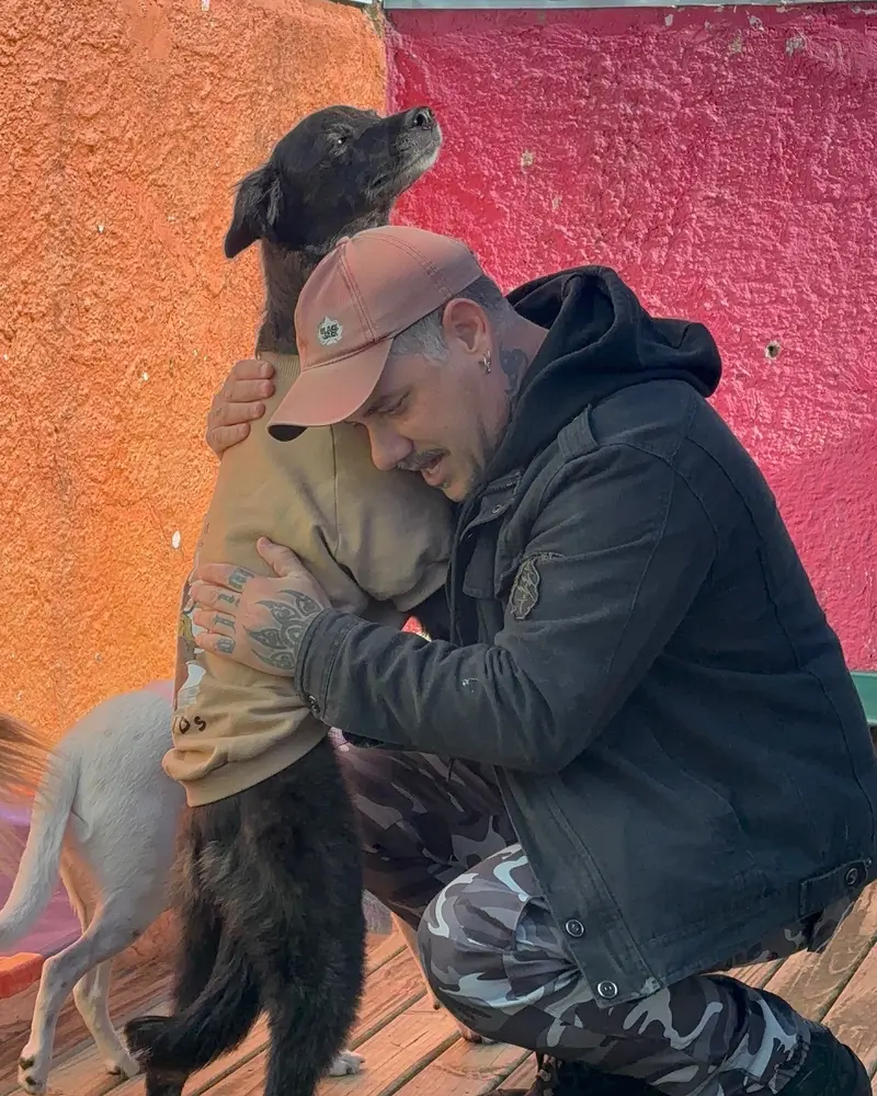 Homem agachado abraçando com carinho um cachorro de pelo escuro
